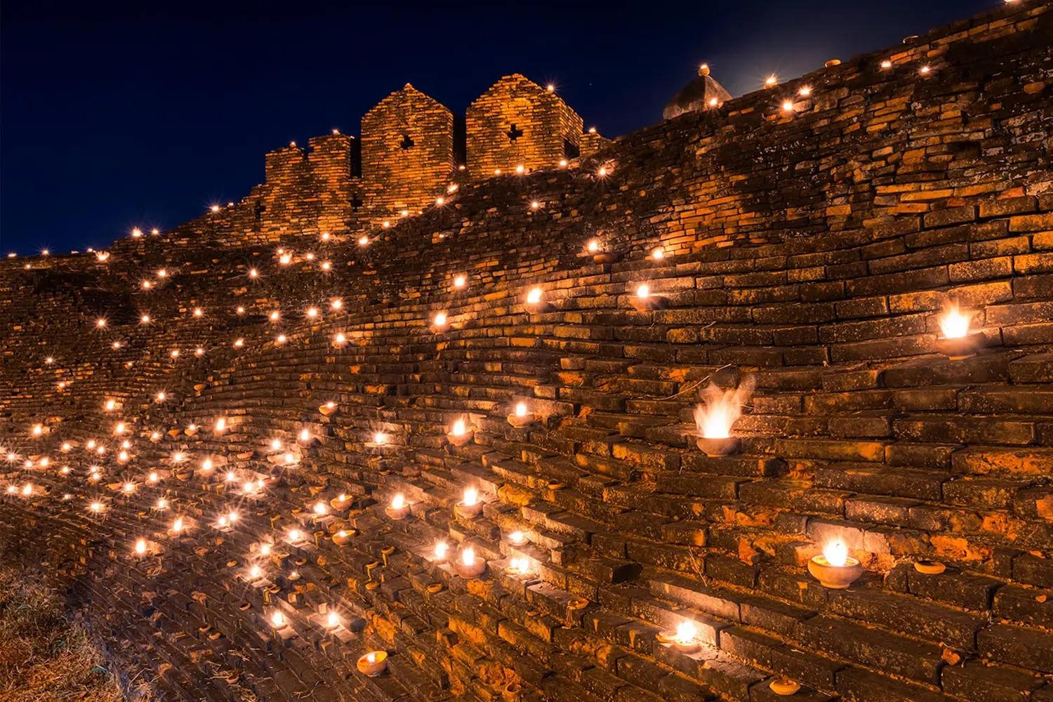 Rows of phang pratip clay oil lamps lit outside a temple in Chiang Mai during Loy Krathong