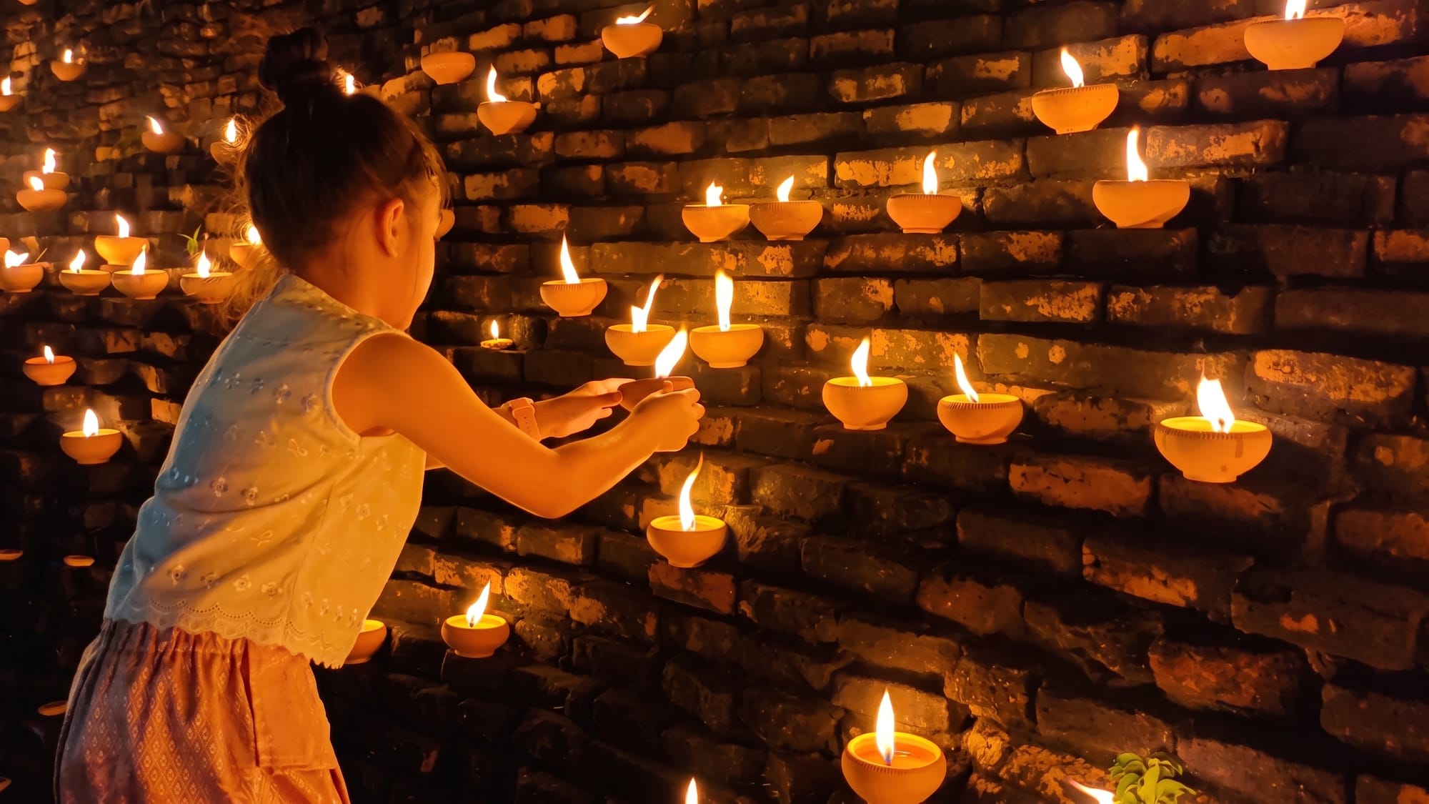 Visitors placing lit phang pratip oil lamps along the old city wall in Chiang Mai